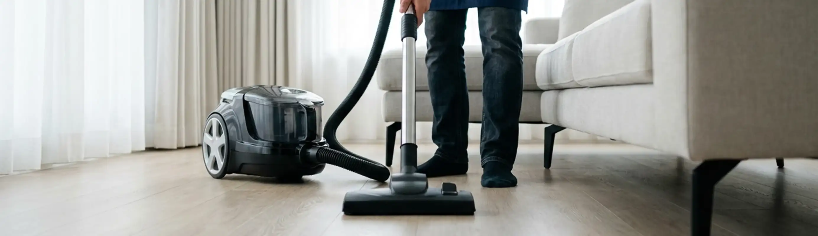 Professional house cleaner vacuuming a living room floor with a canister vacuum cleaner, Orange, CA.