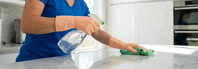Maid service worker spraying and wiping a kitchen countertop with a microfiber cloth for sanitizing, Orange, CA.