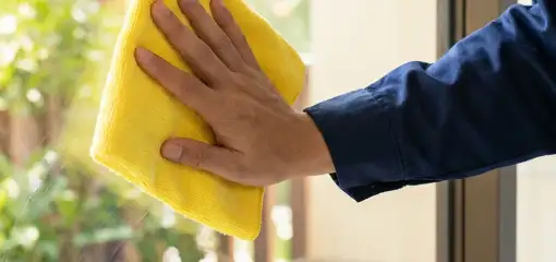 House cleaner wiping a glass window with a yellow microfiber cloth for streak-free cleaning, Orange, CA.